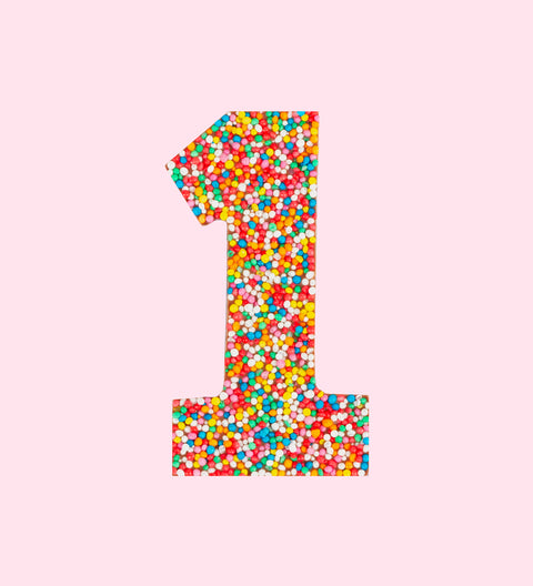 Belgian milk chocolate number 1 shape covered with multicolored sprinkles on a white background