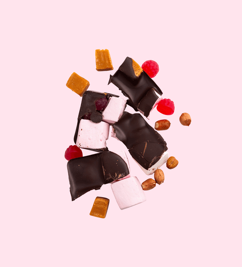 A assortment of chocolate pieces, marshmallows, nuts and fruit pieces arranged on a white background, resembling a rocky road treat.