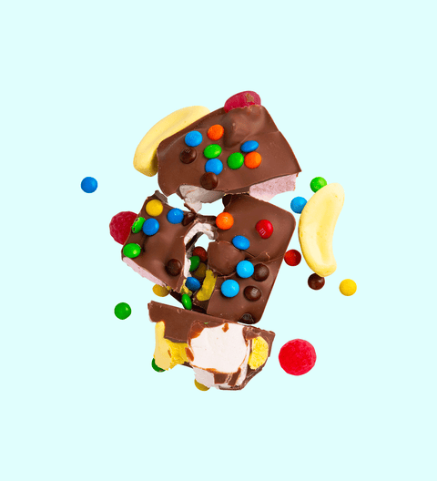 Pieces of rocky road chocolate with visible marshmallows, chocolate chips, and colored candy pieces scattered around.