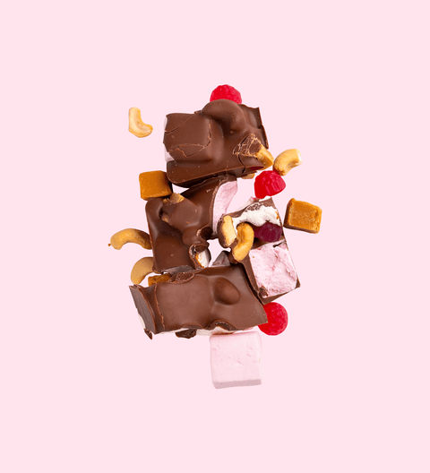 A chocolate bar with pieces of marshmallows, cashews, and caramel fudge visible within the broken pieces.