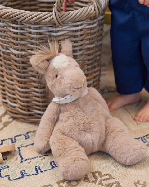 Plush horse toy on a patterned rug with a wicker basket in the background