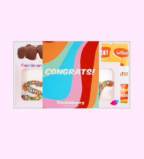 Congratulations gift box, including shapes with messages, milk chocolate pieces, and freckle grab bag, arranged on a white surface with sprinkles and decorative packaging.
