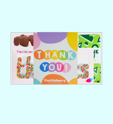 A thank you gift box containing various chocolate treats including a milk chocolate message block, fun rocky road, milk speckles grab bag, mallow pop, and a thanks word. The box is on a white surface with a 'THANK YOU' card beside it.