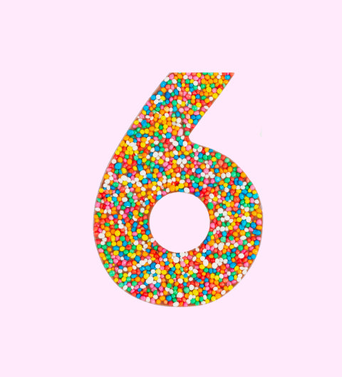 Belgian milk chocolate in the shape of the number 6, covered with multicolored sprinkles on a white background.