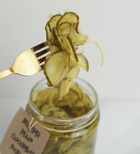 Jar of pickles with a fork holding a pickle spear against a plain background