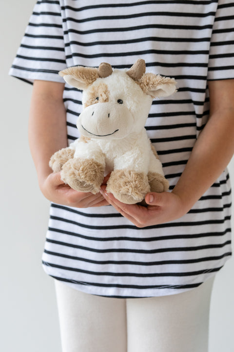 Person holding a plush cow toy against a striped shirt background