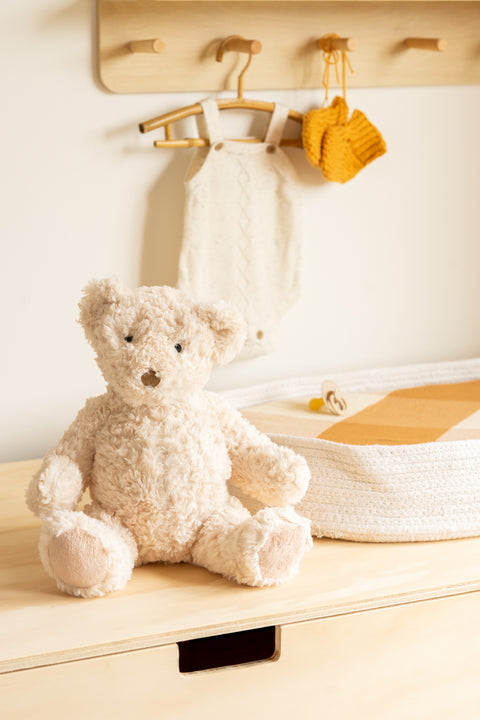 Teddy bear on a wooden surface with a white towel and yellow item hanging in the background.