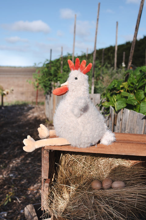 Plush chicken on a wooden bench with hay and eggs in an outdoor setting