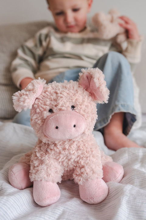 Pink plush pig toy on a blanket with a child in the background