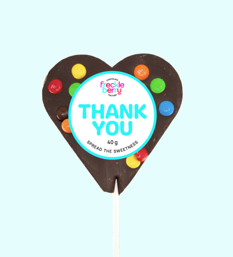 Heart-shaped chocolate lollipop with colorful candies and a 'Thank You' label on a light blue background.