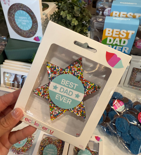 Star-shaped decorative item with 'Best Dad Ever' text in a clear packaging, held in front of a store display.