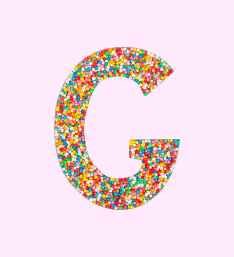 Belgian milk chocolate letter 'G' covered with multicolored sprinkles on a white background