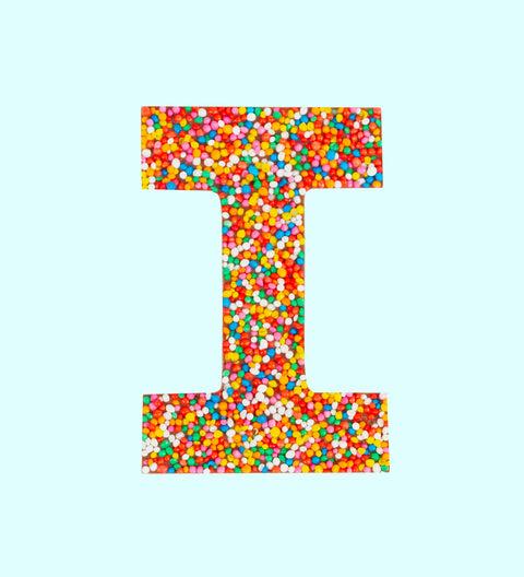Belgian milk chocolate letter 'I' covered with multicolored sprinkles on a white background