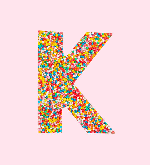 Belgian milk chocolate letter 'K' covered with multicolored sprinkles on a white background