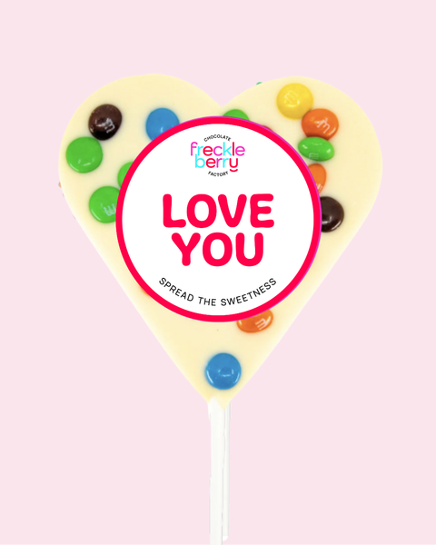 Heart-shaped candy lollipop with colorful candies and 'Freckle Berry' branding on a pink background.