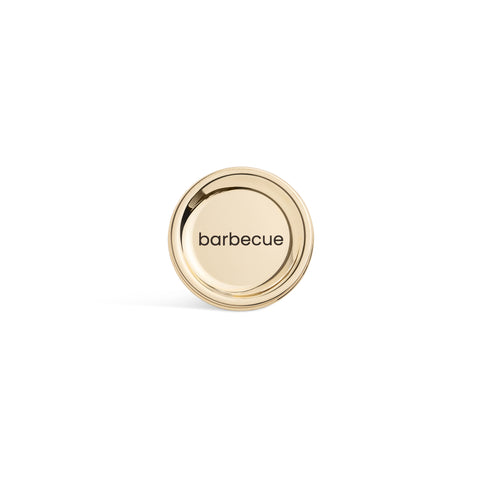 A tall, cylindrical white bottle with a brushed gold label disc at the bottom and a precision squeeze nozzle on the side. Barbecue sauce