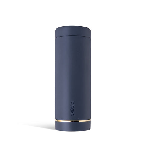 A navy-colored Saucie bottle with a brushed gold label disc at the bottom, designed for dispensing sauces.