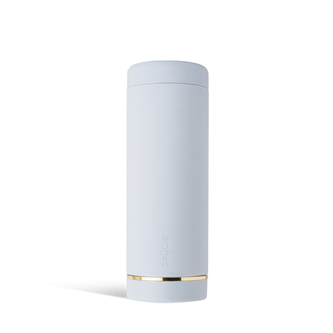 A tall, cylindrical blue Saucie bottle with a brushed gold label disc at the bottom and a gold lid on top, designed for dispensing sauces.