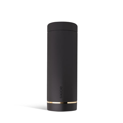 A tall, black, cylindrical Saucie bottle with a brushed gold label disc near the bottom.