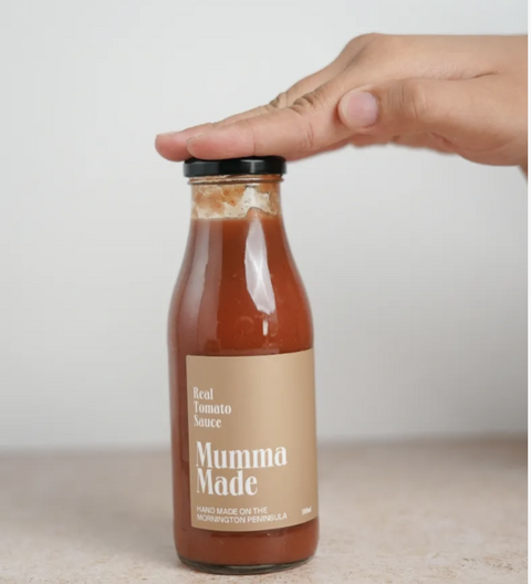 Bottle of 'Mumma Made' real tomato sauce with a hand lifting the lid against a neutral background