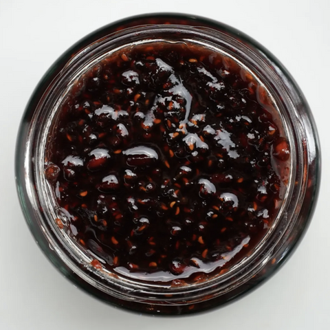 Close-up of a jar of dark berry jam on a white background
