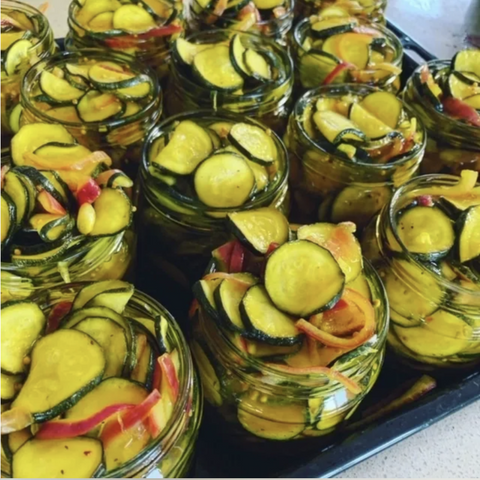 Jars of pickled vegetables including zucchini and peppers on a tray.