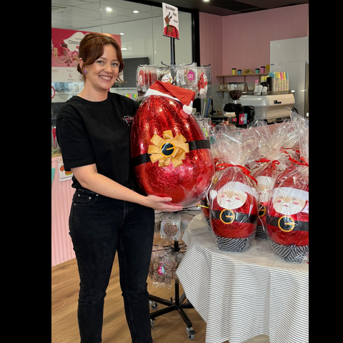 Person holding a large red Christmas egg with a Santa Claus design in a store setting.