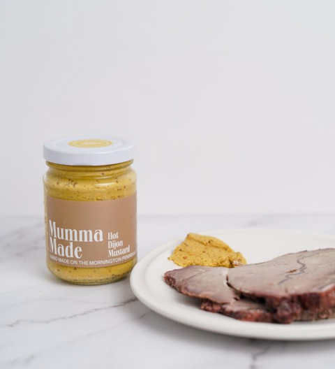 Jar of 'Mumma Made' hot dijon mustard on a marble surface with slices of meat.