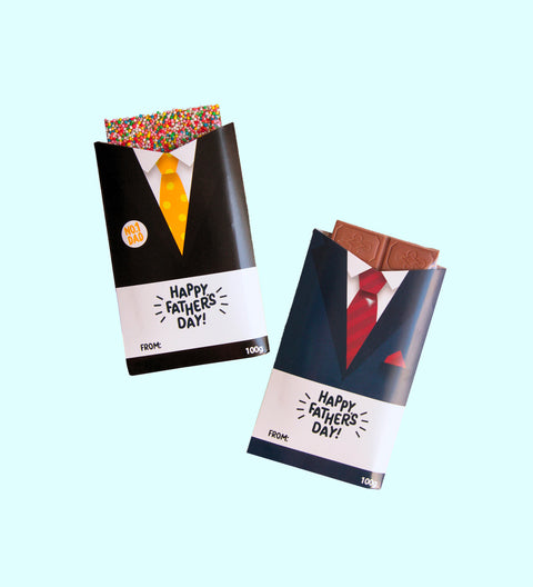 Two chocolate blocks wrapped in Father's Day themed wrappers, one in black and one in blue, with 'Happy Father's Day' text and suit designs.