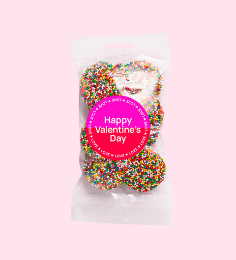 A clear plastic bag filled with multicolored chocolate freckles, sealed with a pink label that reads 'Happy Valentine's Day'.
