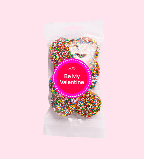 A clear plastic bag filled with multicolored chocolate freckles, sealed with a pink label that reads 'Happy Valentine's Day'.