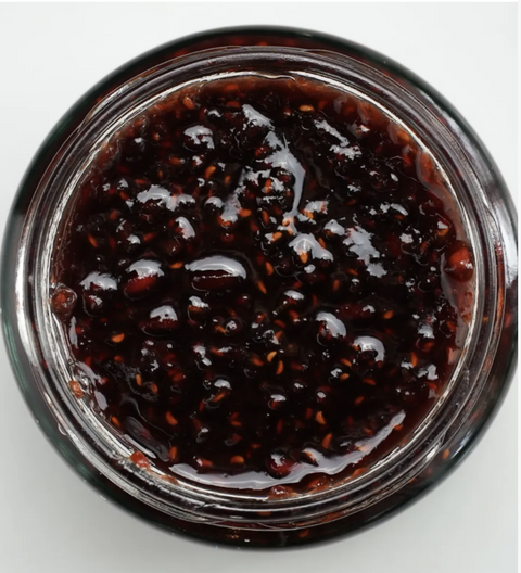 Close-up of a jar of dark berry jam on a white background