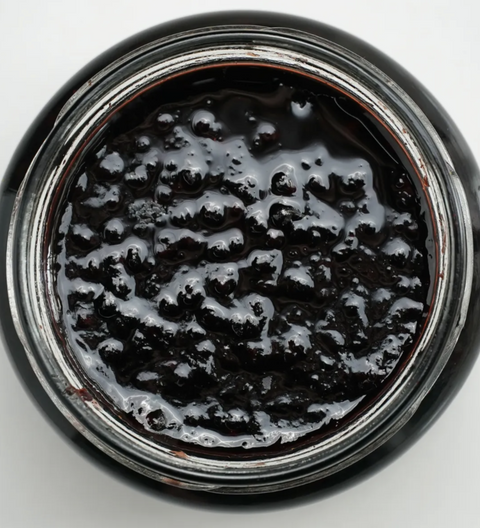 Close-up of a jar with dark, thick substance inside on a white background