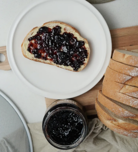 Toast with jam on a white plate, jar of jam, and sliced bread on a wooden board. gifts and jams and chutneys
