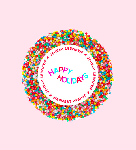 Individually wrapped chocolate freckle with 'Happy Holidays' text in the center, surrounded by colorful sprinkles on a pink background.