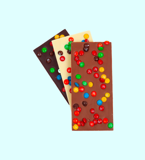A selection of chocolate blocks with Mini M&M's candies on top, presented in milk, dark, and white varieties.