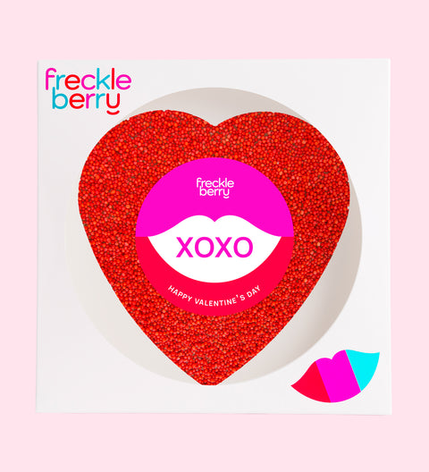 A large, heart-shaped piece of Belgian chocolate covered in red colored sprinkles, with a 'FRECKLE XOXO HAPPY VALENTINE'S DAY' sticker on top.