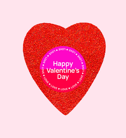 A large, heart-shaped piece of Belgian chocolate covered in red colored sprinkles, with a 'FRECKLE XOXO HAPPY VALENTINE'S DAY' sticker on top.