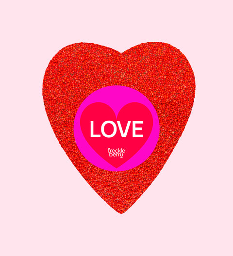 A large, heart-shaped piece of Belgian chocolate covered in red colored sprinkles, with a 'FRECKLE XOXO HAPPY VALENTINE'S DAY' sticker on top.