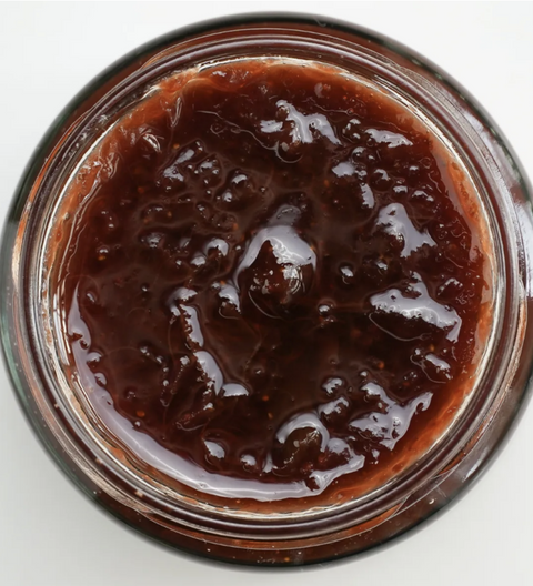 Close-up of a jar of dark brown jam on a white background