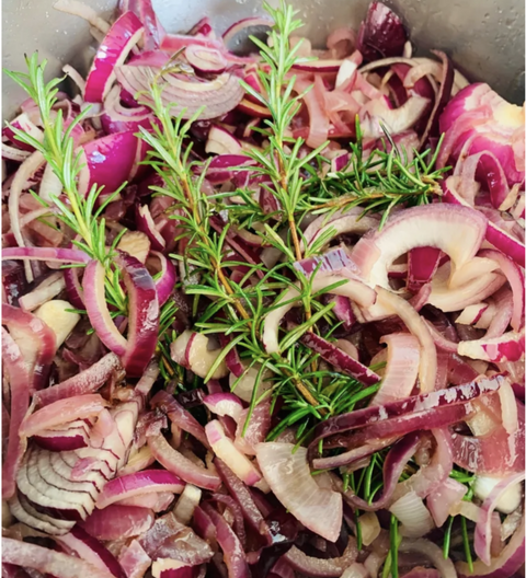 Sliced red onions with rosemary on a metal surface