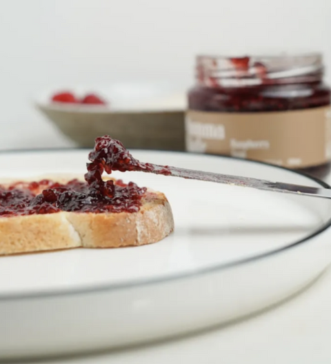 Jelly on bread with a jar of jelly in the background the best raspberry jam