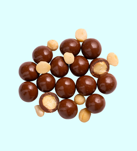 A collection of milk chocolate coated macadamia nuts with a few nuts partially coated in chocolate.