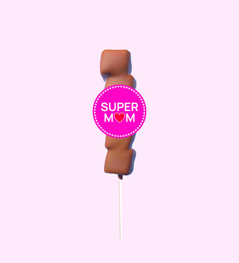A marshmallow lollipop with a 'SUPER MOM' text badge, covered in Belgian milk chocolate drizzle on a pink background.