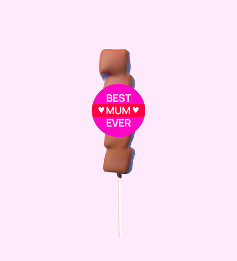 A marshmallow lollipop with a 'SUPER MOM' text badge, covered in Belgian milk chocolate drizzle on a pink background.