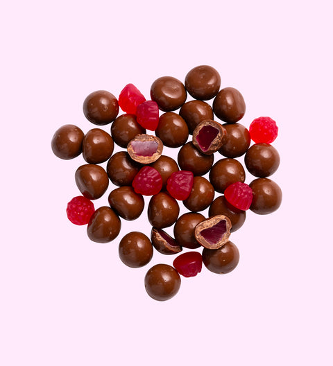 A collection of milk chocolate coated raspberries with a few raspberries removed from the chocolate coating to reveal the fruit inside.