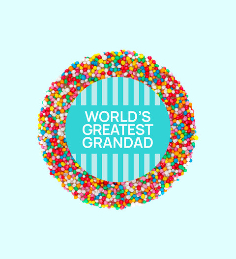 A chocolate freckle with 'WORLD'S GREATEST GRANDAD' written in the center, against a blue striped background.