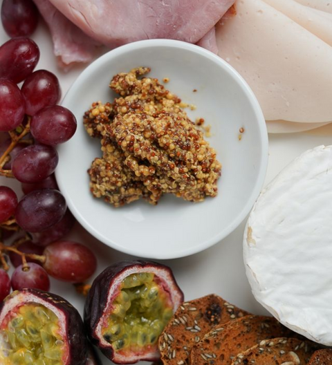 Small bowl of crumbled cheese with grapes, cured meats, and a wheel of cheese on a platter.