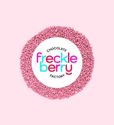 A circular pink freckle candy on a pink background, individually wrapped.