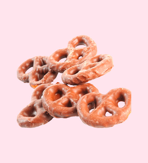 A group of milk chocolate covered pretzels against a pink background.